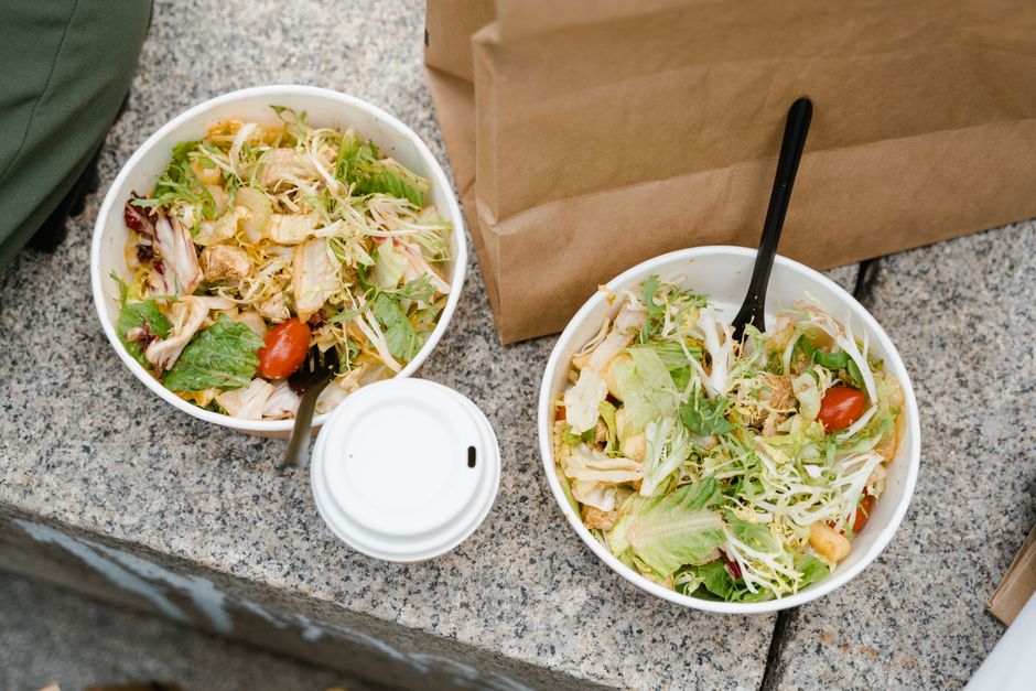 Two takeaway salads with vegetables and chicken on an outdoor surface, showcasing fresh and healthy food.